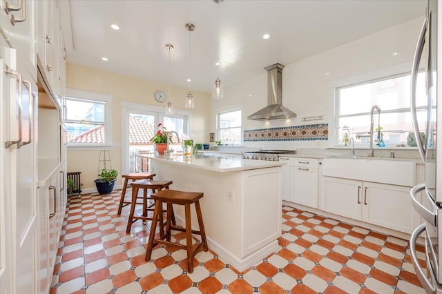 kitchen featuring a breakfast bar area, light floors, a kitchen island, light countertops, and wall chimney exhaust hood