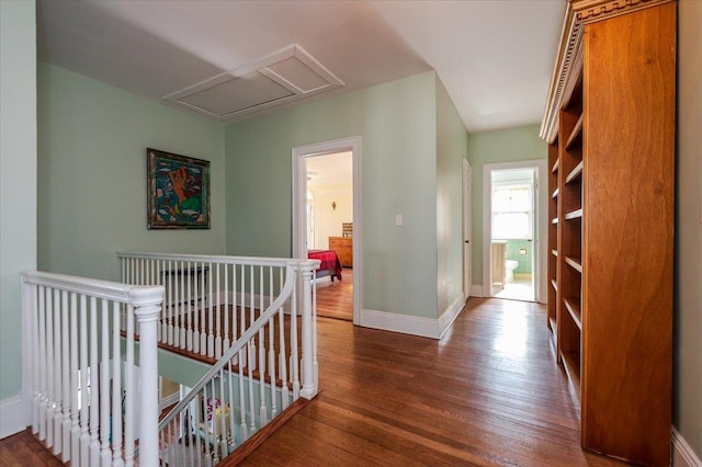 corridor featuring baseboards, wood finished floors, an upstairs landing, and attic access