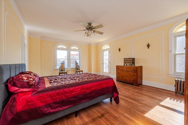 bedroom with a decorative wall, wood finished floors, baseboards, ornamental molding, and radiator