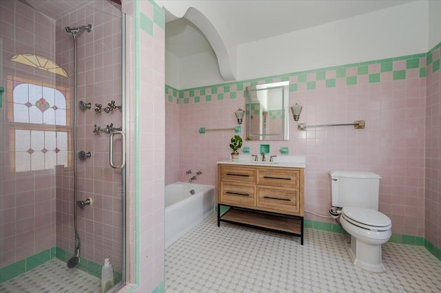 bathroom featuring a stall shower, toilet, a bath, vanity, and tile walls