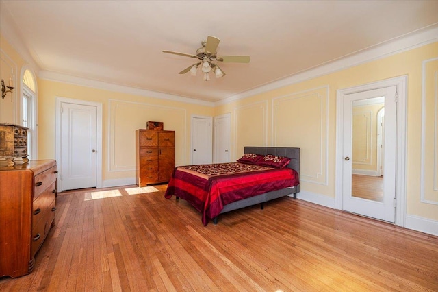 bedroom featuring crown molding, light wood-style flooring, a decorative wall, and ceiling fan