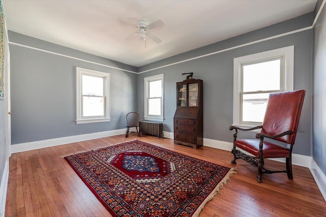 sitting room with hardwood / wood-style floors, radiator heating unit, a ceiling fan, and baseboards