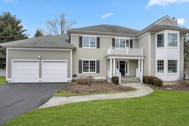 view of front of property with a shingled roof, an attached garage, a front yard, a balcony, and driveway