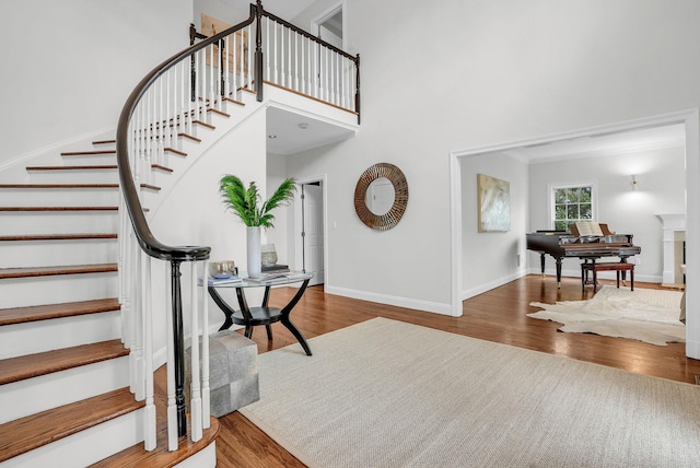 foyer with a fireplace, a towering ceiling, wood finished floors, baseboards, and stairs