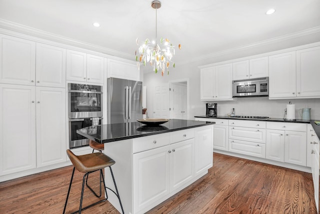 kitchen with appliances with stainless steel finishes, dark countertops, a center island, and wood finished floors