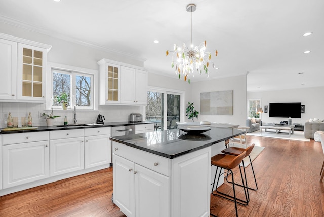 kitchen featuring decorative backsplash, dark countertops, light wood-style flooring, a kitchen bar, and a sink