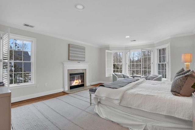 bedroom with baseboards, visible vents, a glass covered fireplace, wood finished floors, and crown molding