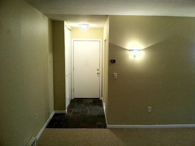 hall with dark colored carpet and baseboards