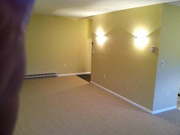 carpeted empty room with a baseboard heating unit and baseboards