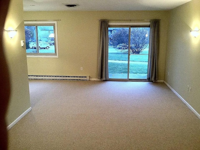 empty room with a baseboard heating unit, carpet, visible vents, and baseboards