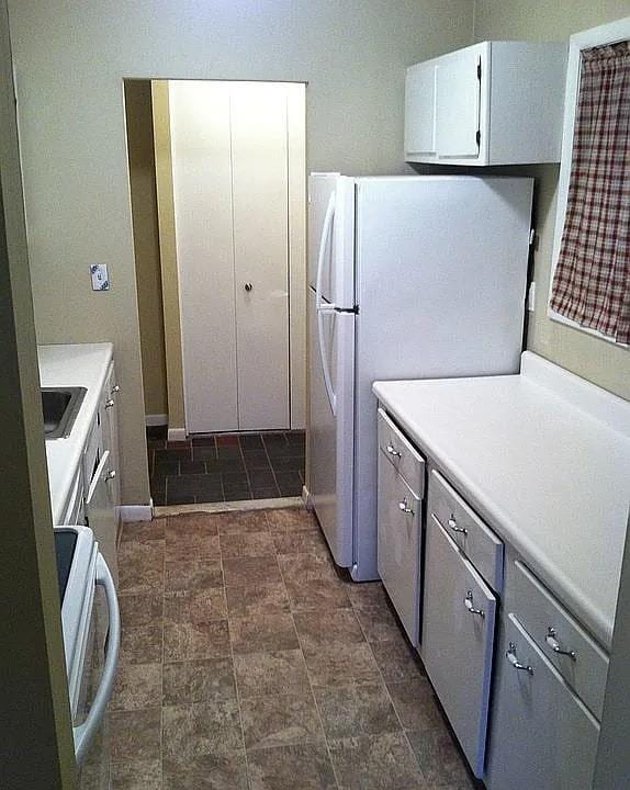 kitchen featuring washer / dryer, baseboards, freestanding refrigerator, light countertops, and white cabinetry