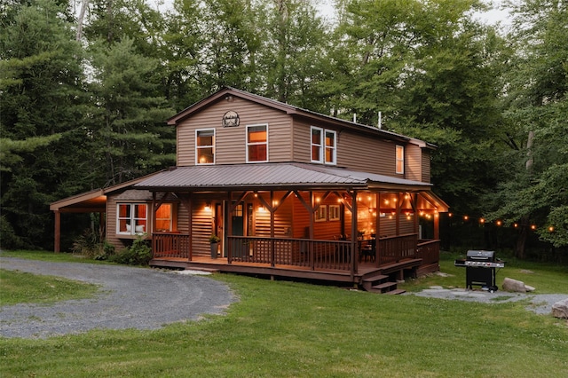 view of front of home with gravel driveway, metal roof, a porch, and a front yard