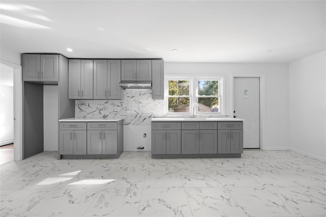 kitchen with gray cabinets, a sink, marble finish floor, and decorative backsplash