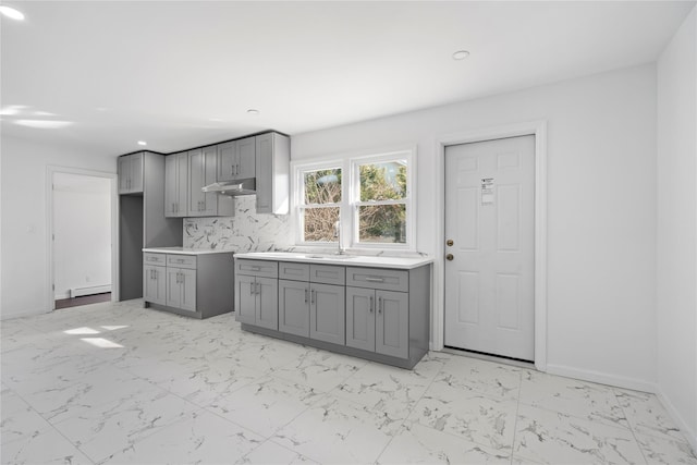 kitchen with gray cabinets, under cabinet range hood, baseboards, and marble finish floor