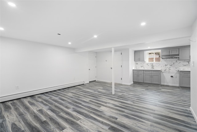 unfurnished living room featuring a baseboard heating unit, baseboards, wood finished floors, and recessed lighting