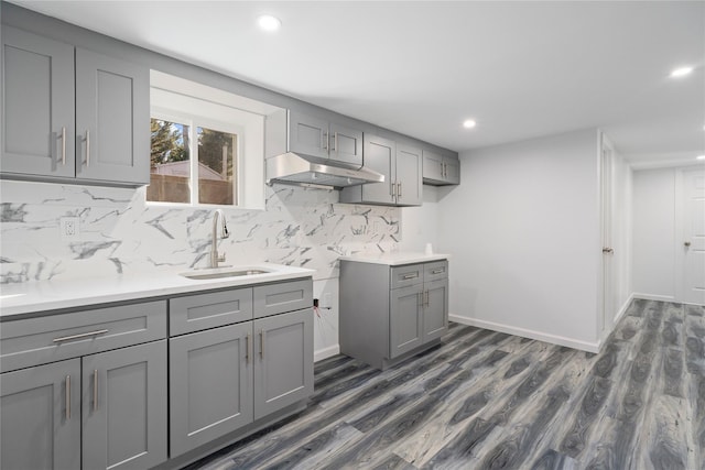 kitchen with tasteful backsplash, dark wood-type flooring, gray cabinetry, under cabinet range hood, and a sink