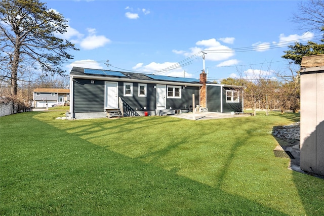 back of house with entry steps, a lawn, a patio, a chimney, and roof mounted solar panels