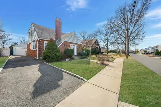 view of side of home with a chimney, a detached garage, an outbuilding, a yard, and brick siding