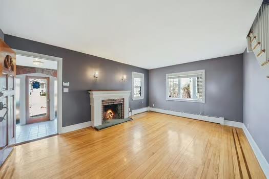 unfurnished living room featuring a brick fireplace, baseboards, baseboard heating, and wood finished floors