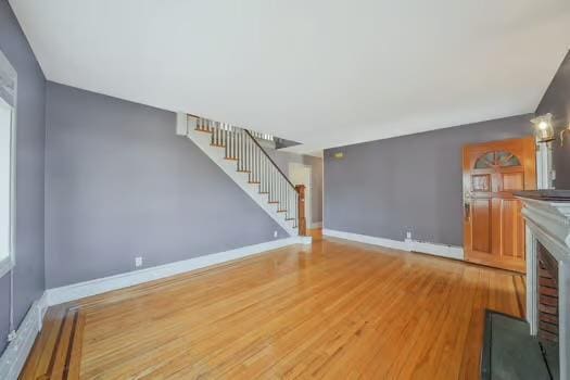 unfurnished living room with stairway, a brick fireplace, wood finished floors, and baseboards