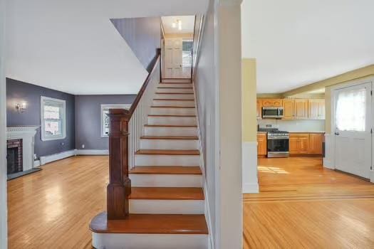 staircase featuring a baseboard heating unit, a fireplace, baseboards, and wood finished floors