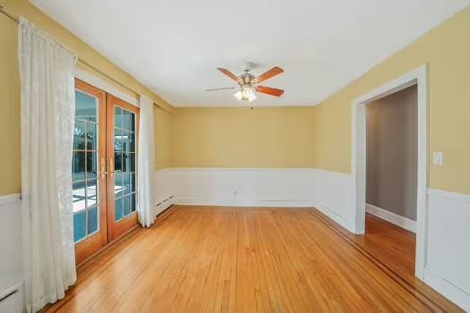 spare room with wainscoting, a baseboard heating unit, wood finished floors, and french doors