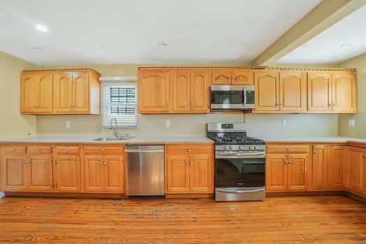 kitchen with light wood-style floors, stainless steel appliances, a sink, and light countertops