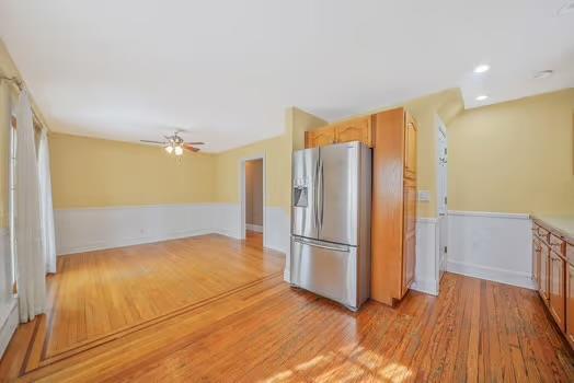 kitchen featuring a ceiling fan, a wainscoted wall, light wood-style flooring, and stainless steel fridge with ice dispenser