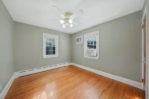 unfurnished room with a baseboard heating unit, plenty of natural light, wood finished floors, and baseboards