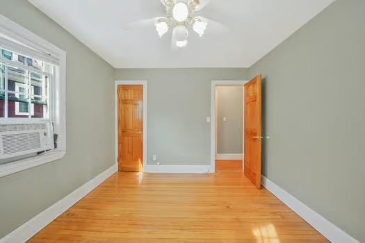 unfurnished bedroom featuring a ceiling fan, cooling unit, baseboards, and wood finished floors