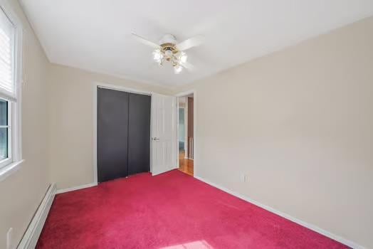 unfurnished bedroom with a baseboard radiator, a closet, multiple windows, and carpet flooring