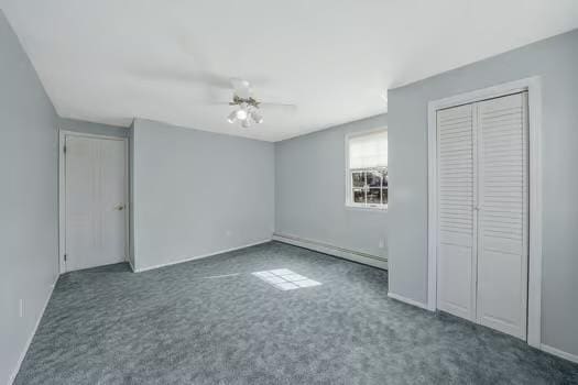 unfurnished bedroom with a ceiling fan, dark colored carpet, a closet, and a baseboard heating unit