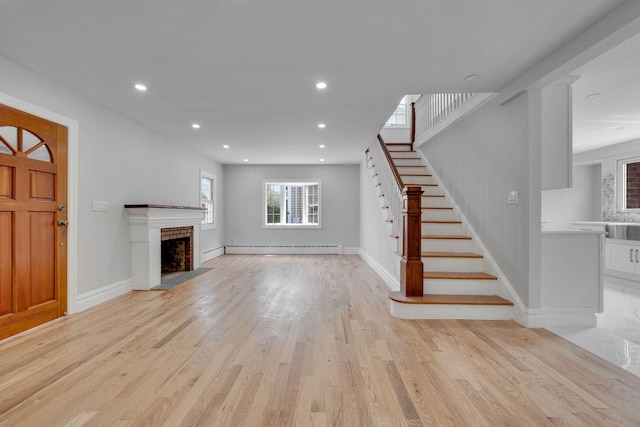 unfurnished living room with a fireplace with raised hearth, recessed lighting, stairs, and light wood-type flooring