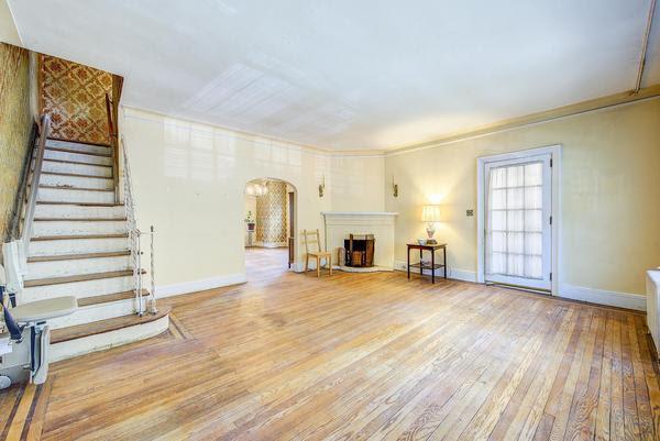 unfurnished living room with arched walkways, a fireplace with raised hearth, stairway, light wood-style floors, and baseboards