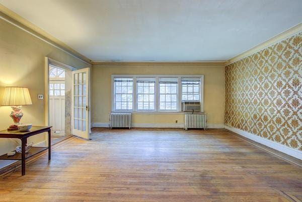 unfurnished room with crown molding, wallpapered walls, baseboards, and radiator