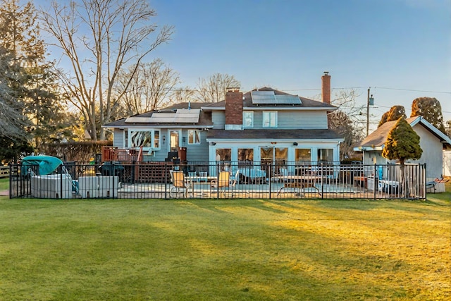 rear view of property with fence, a lawn, a pool, and solar panels