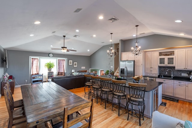 dining room featuring visible vents, vaulted ceiling, light wood-style flooring, and ceiling fan with notable chandelier