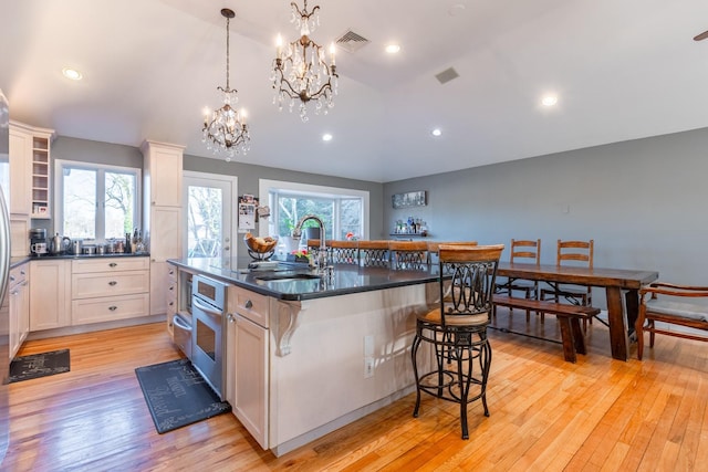 kitchen featuring visible vents, hanging light fixtures, a kitchen island with sink, a sink, and a kitchen bar