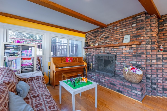 living room featuring a brick fireplace, brick wall, beam ceiling, and wood finished floors