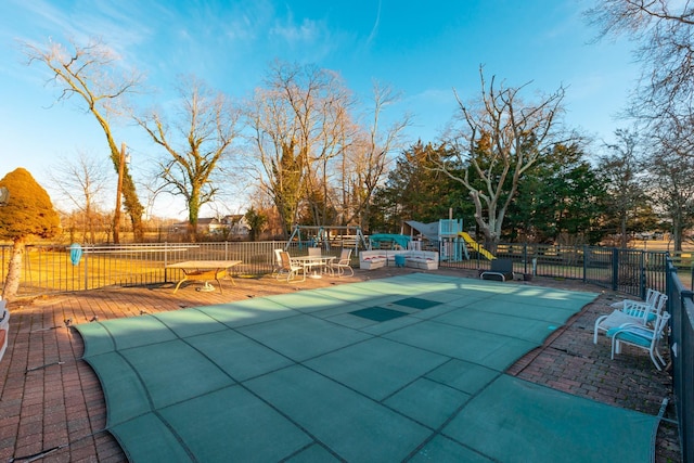 view of pool with outdoor dining area, playground community, fence, and a patio