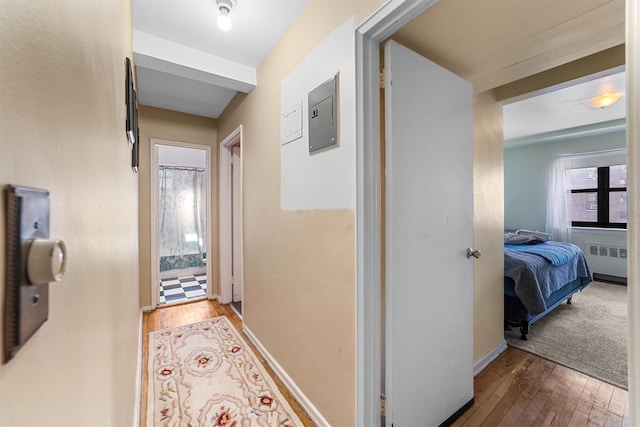 corridor with baseboards, wood-type flooring, electric panel, and radiator