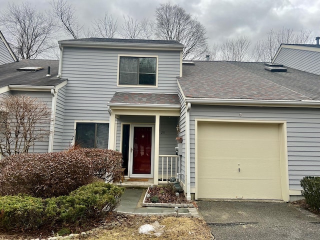 traditional home featuring aphalt driveway, an attached garage, and a shingled roof