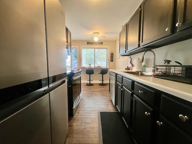 kitchen with stainless steel appliances, light countertops, a sink, wood finished floors, and baseboards