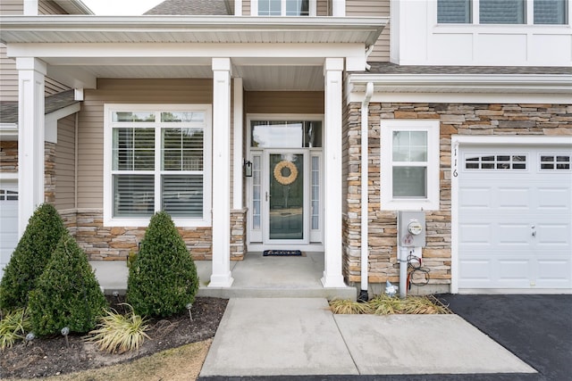 entrance to property featuring a garage, stone siding, and roof with shingles