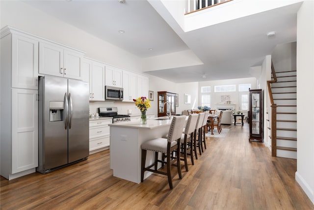 kitchen with an island with sink, dark wood-style floors, a breakfast bar, stainless steel appliances, and white cabinetry