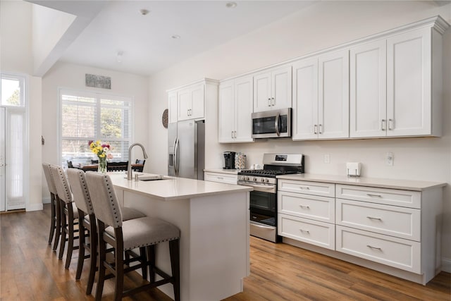 kitchen with a breakfast bar area, a sink, appliances with stainless steel finishes, dark wood finished floors, and a center island with sink