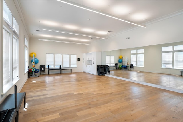 workout room with a towering ceiling, light wood-style flooring, ornamental molding, and baseboards