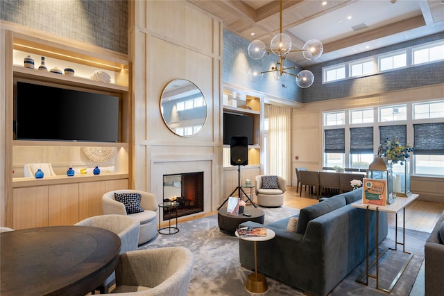 living room featuring coffered ceiling, a towering ceiling, a premium fireplace, an inviting chandelier, and built in shelves