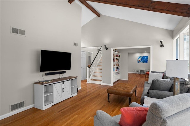 living room featuring stairway, beamed ceiling, visible vents, and light wood-type flooring