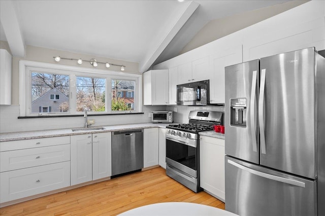 kitchen with a sink, backsplash, appliances with stainless steel finishes, white cabinets, and lofted ceiling